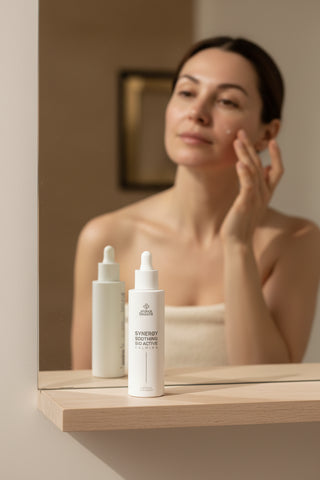 Synergy Soothing Alissa Beauté 50 ml pe raftul din baie, iar în fundal o femeie aplică serul calmant pe pometi